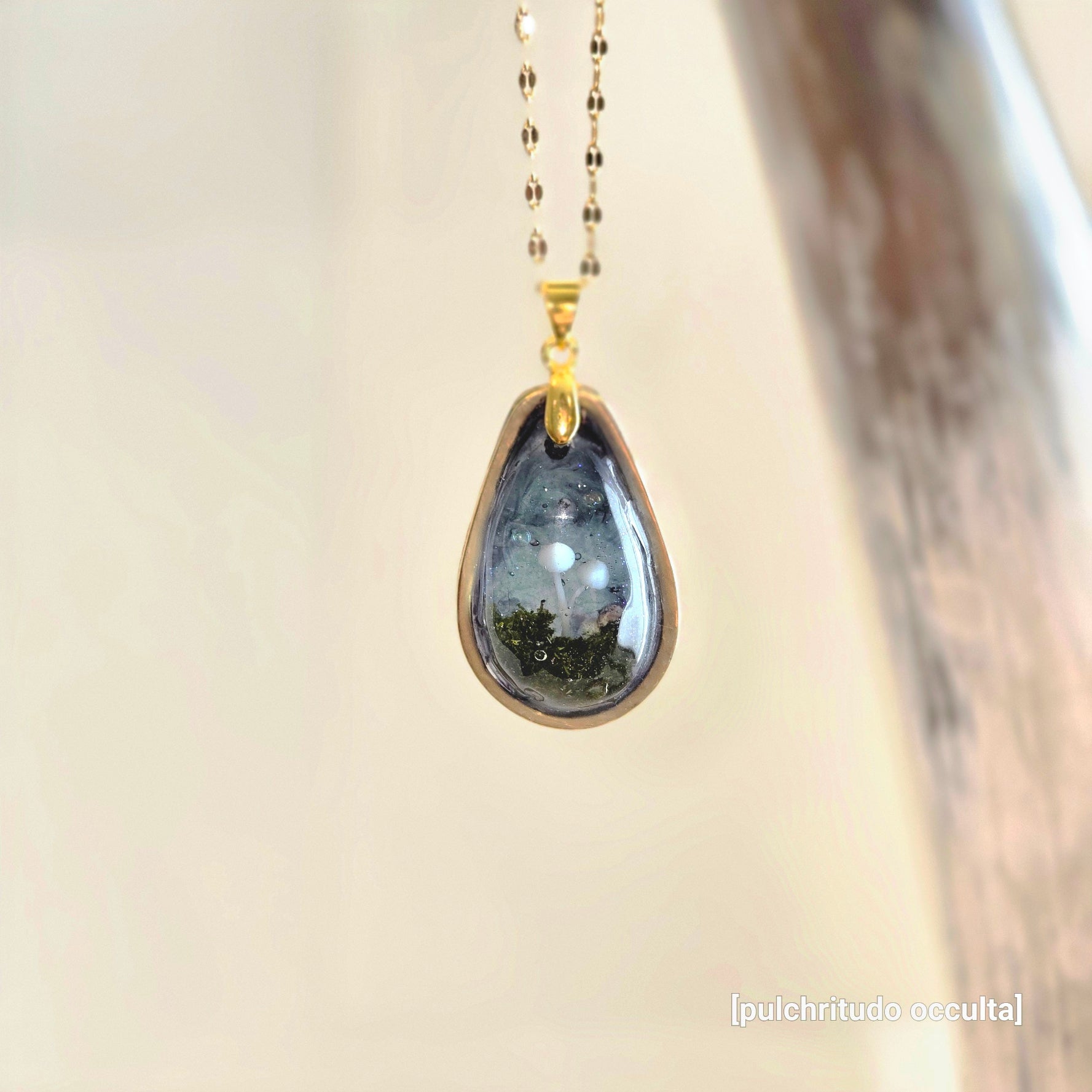 Teardrop-shaped pendant with gold chain on a neutral background