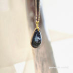 Teardrop-shaped pendant with gold chain on a light background