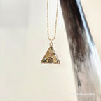 Necklace with a triangular pendant hanging from a large horn on a light background
