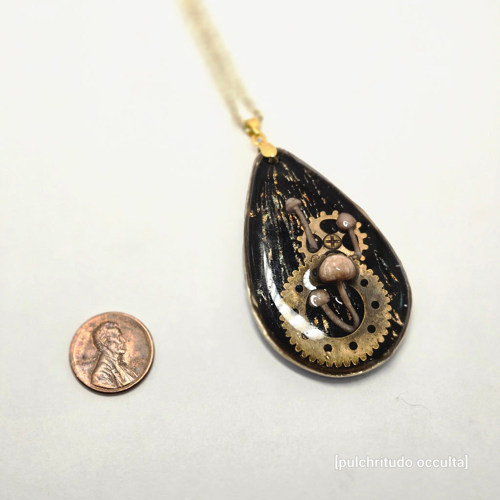 Decorative pendant with steampunk design next to a penny on a white background