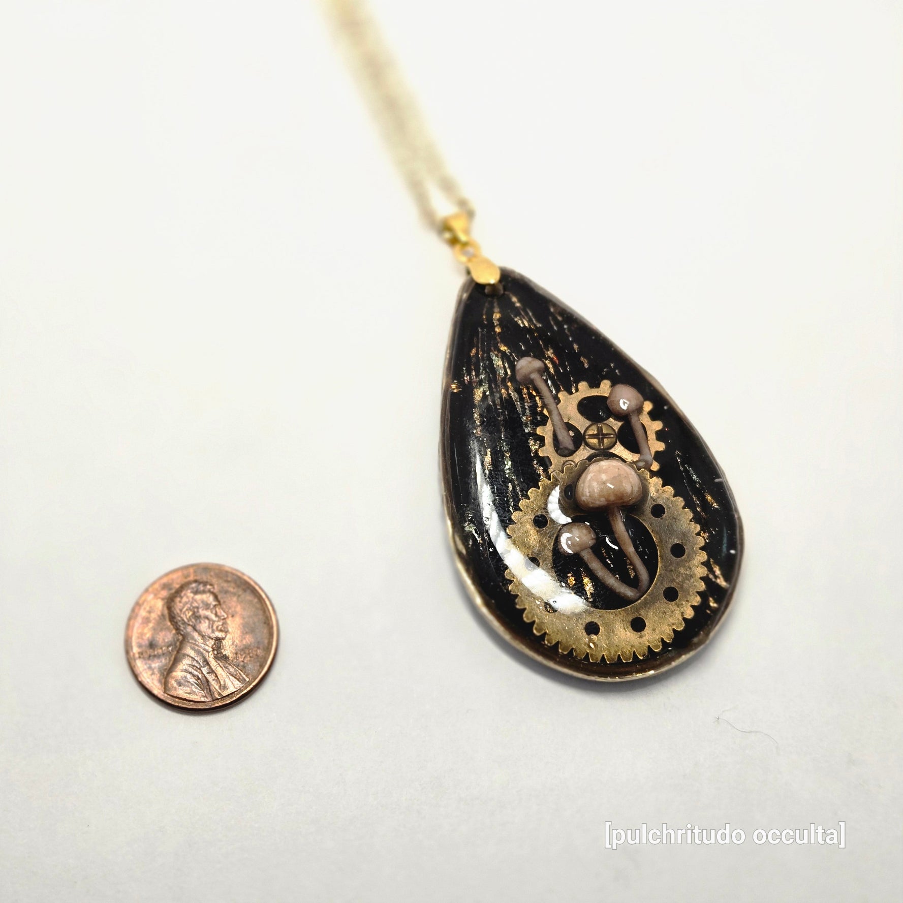Decorative pendant with steampunk design next to a penny on a white background