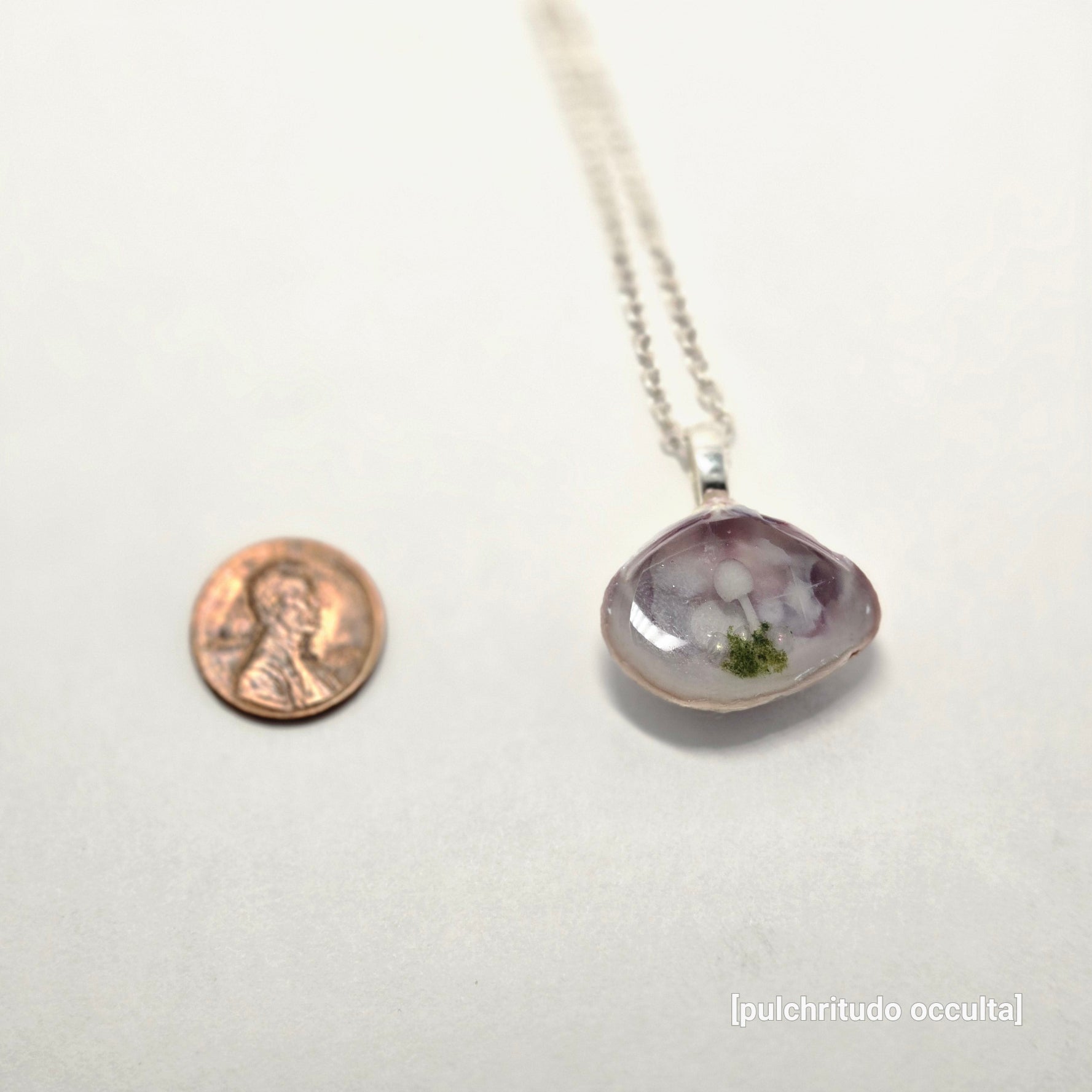 Necklace with a pendant next to a penny on a white background