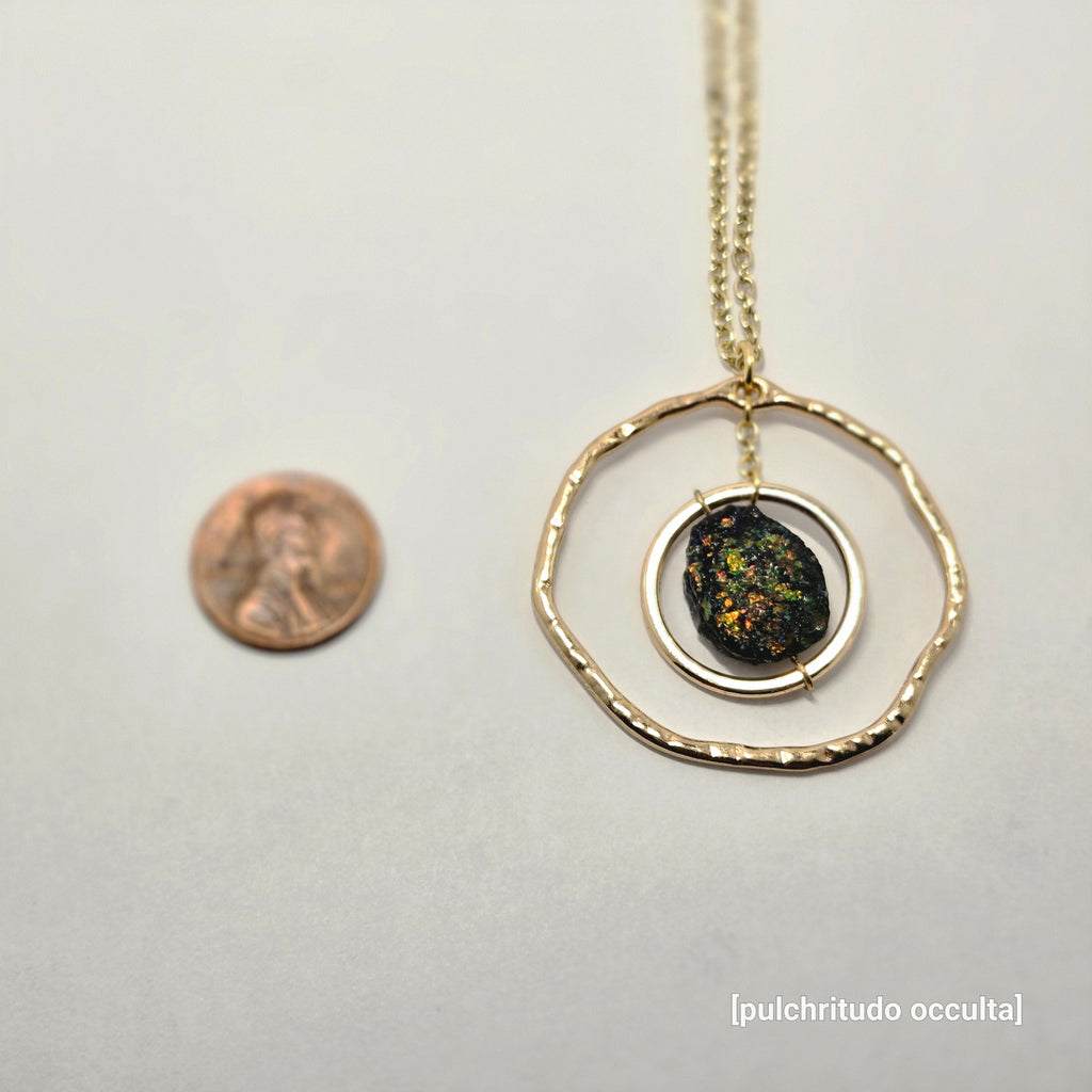 Necklace with a circular pendant on a white background, next to a penny for scale.