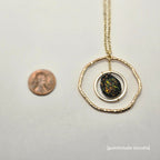 Necklace with a circular pendant on a white background, next to a penny for scale.