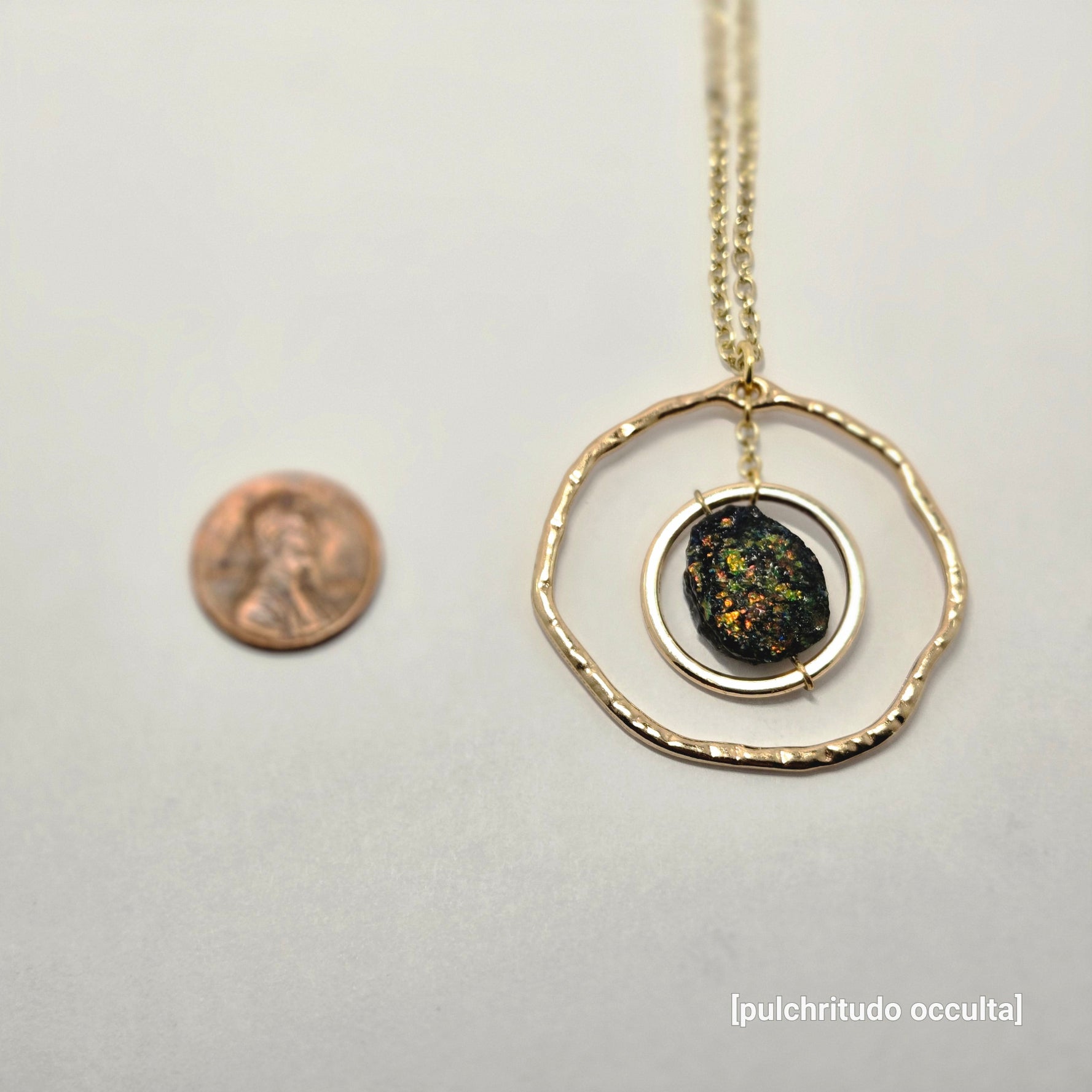 Necklace with a circular pendant on a white background, next to a penny for scale.