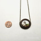 Necklace with a round pendant next to a penny on a white background