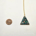 Necklace with a triangular pendant on a white background, next to a penny for scale.