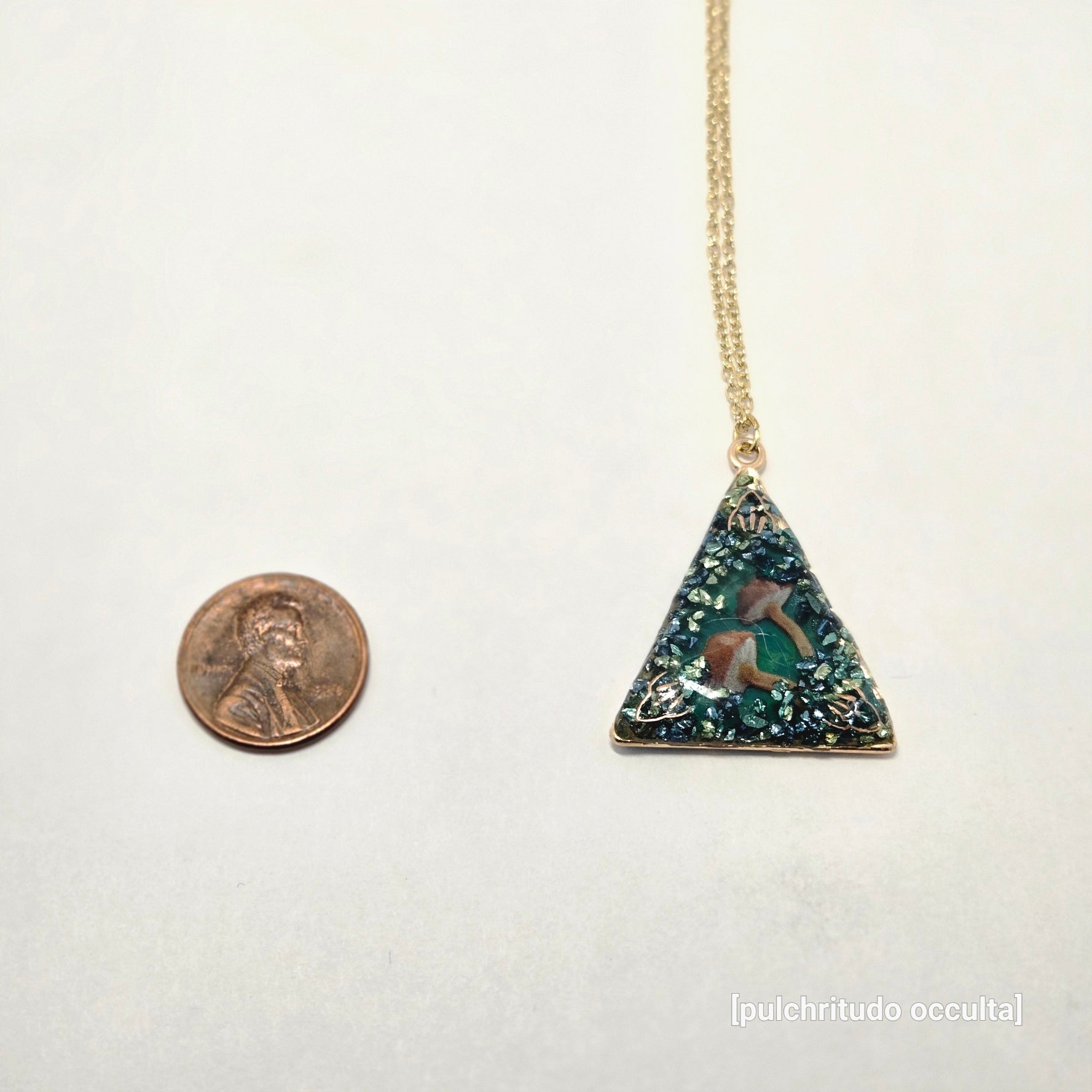 Necklace with a triangular pendant on a white background, next to a penny for scale.