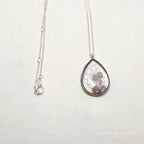 Silver necklace with a teardrop-shaped pendant on a light gray background