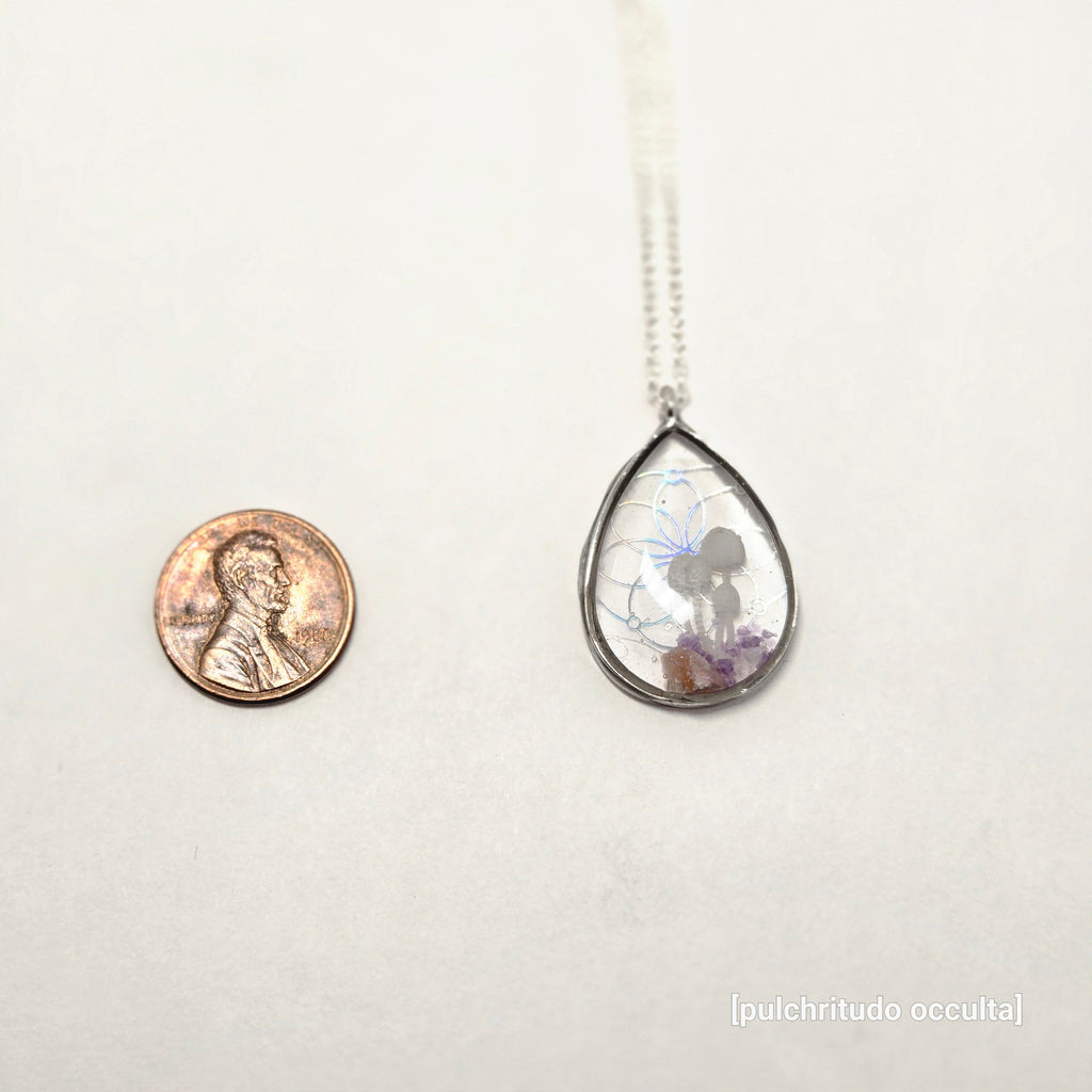 Teardrop-shaped pendant with a coin underneath on a white background