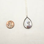 Teardrop-shaped pendant with a coin underneath on a white background