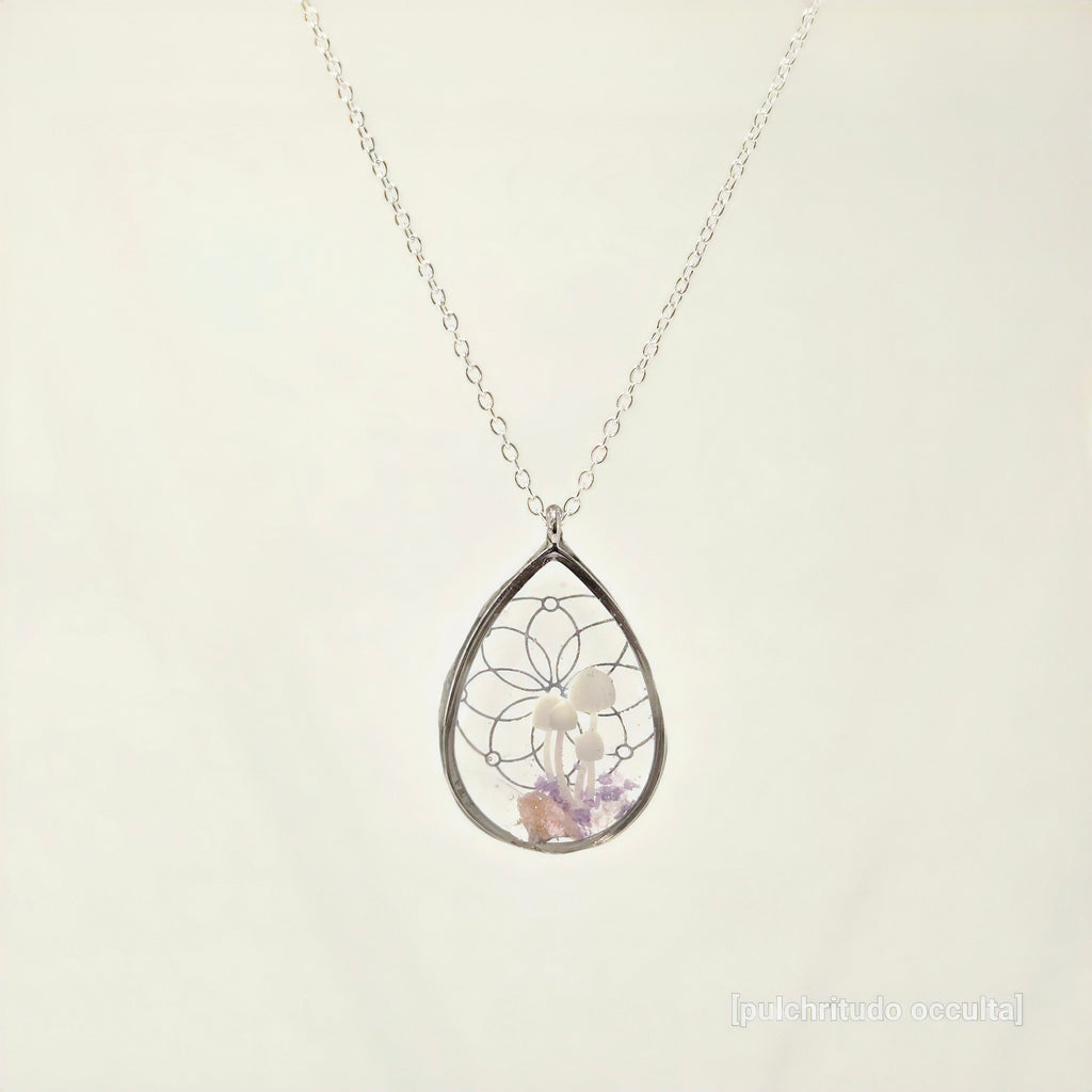 Teardrop-shaped silver pendant with embedded stones on a light beige background