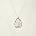 Teardrop-shaped silver pendant with embedded stones on a light beige background