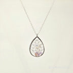 Teardrop-shaped silver pendant with embedded stones on a light beige background
