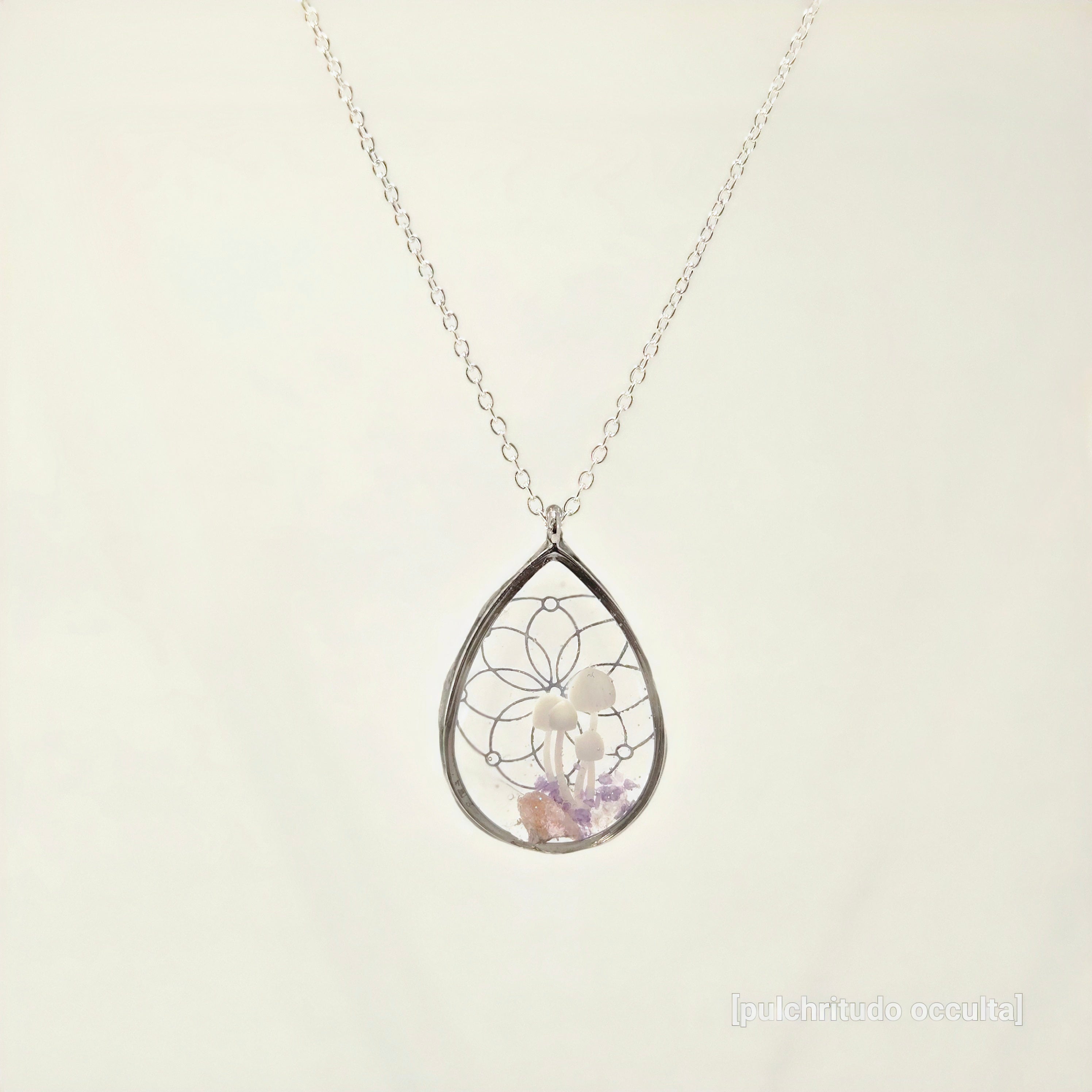 Teardrop-shaped silver pendant with embedded stones on a light beige background