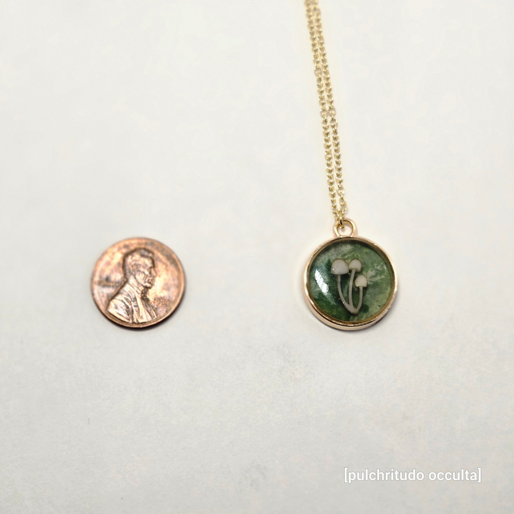 Small green pendant necklace on a white background with a penny for scale.