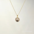 Gold necklace with a circular pendant on a light gray background
