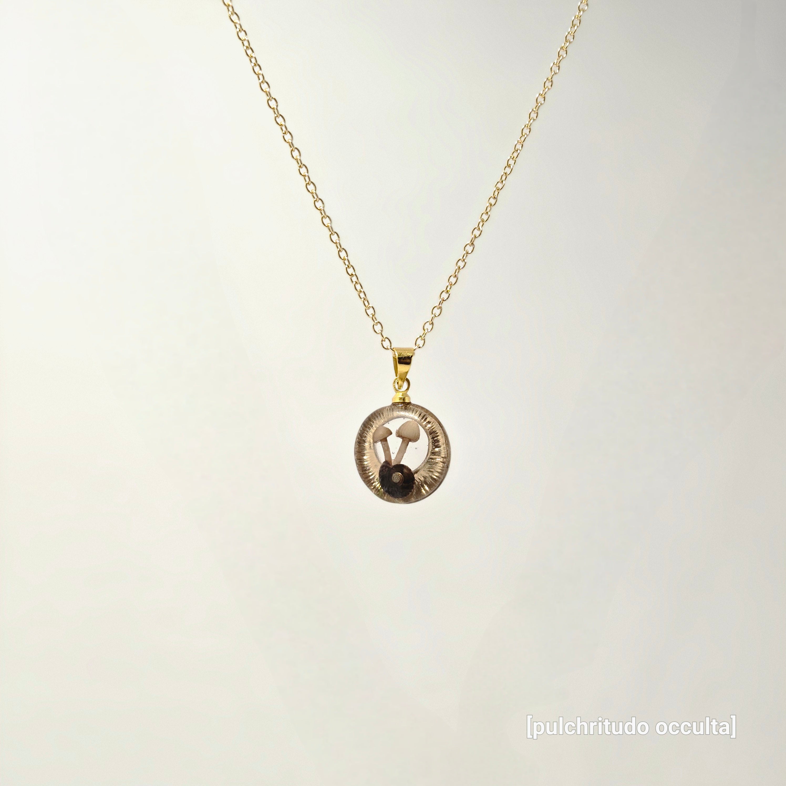 Gold necklace with a circular pendant on a light gray background