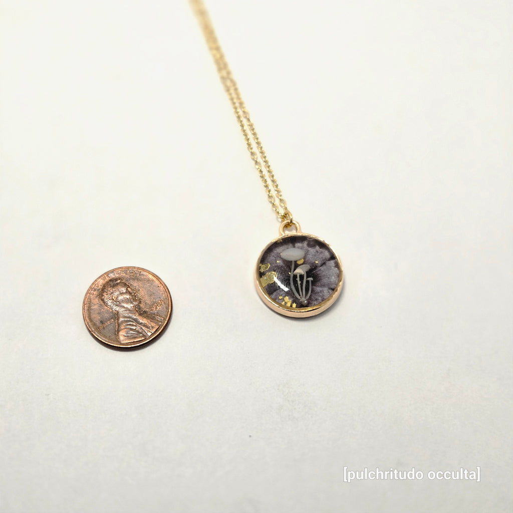 Necklace with a circular pendant on a white background, next to a penny for scale.