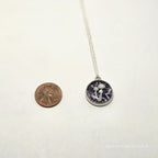 Small round pendant with chain on a white background, next to a penny for scale.