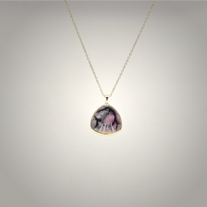 A gold chain necklace with a teardrop-shaped pendant featuring a pink and black marbled pattern, set in a gold bezel against a light gray gradient background.