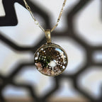 A round resin pendant necklace containing a tiny white mushroom, green moss, and small stones over a delicate lace‑leaf background, hanging from a 24‑inch antique‑gold chain.