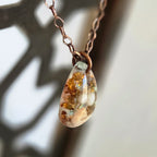 Teardrop-shaped pendant necklace with a blurred natural background