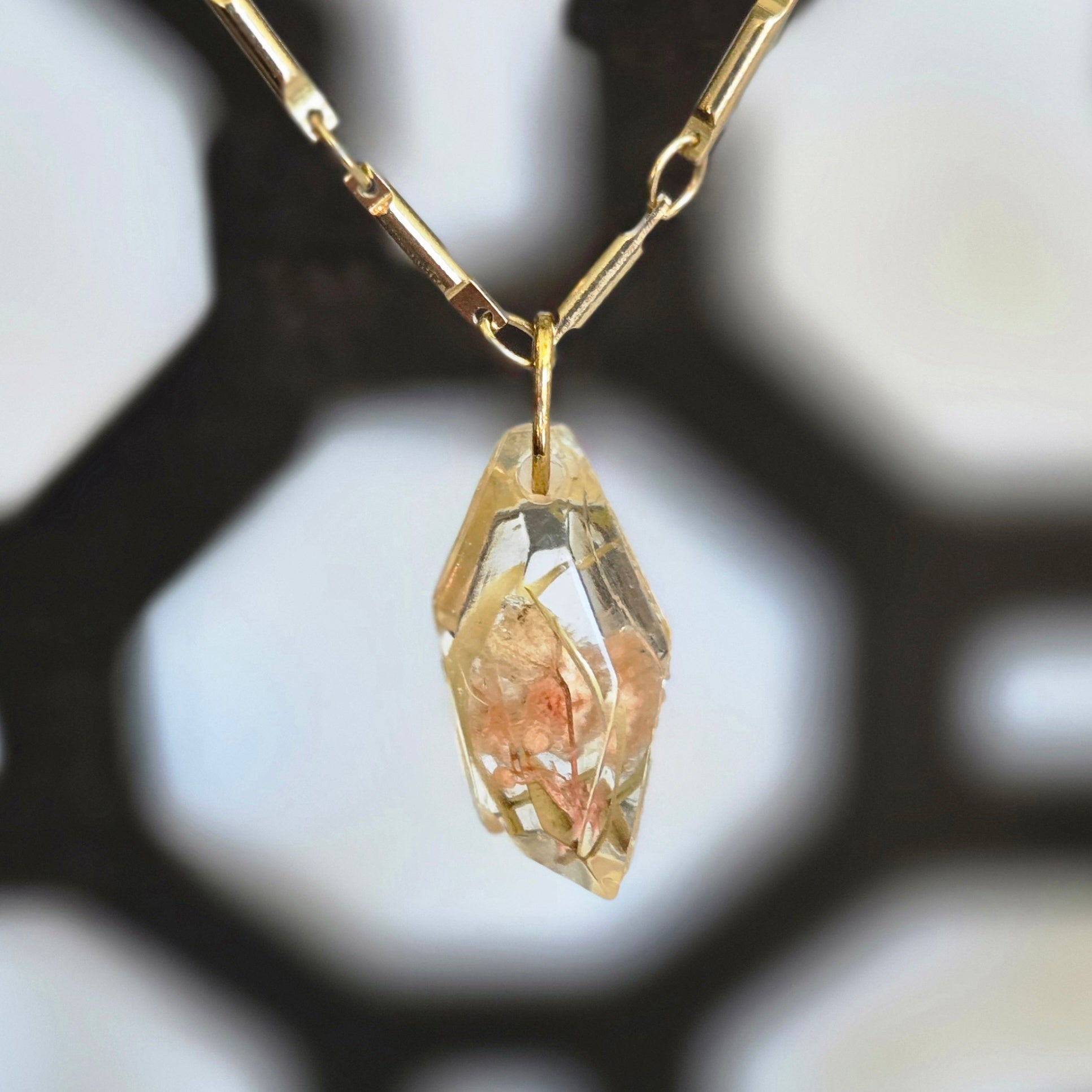A faceted clear resin pendant containing a soft pink flower inclusion, hanging from a 19‑inch gold‑tone chain.
