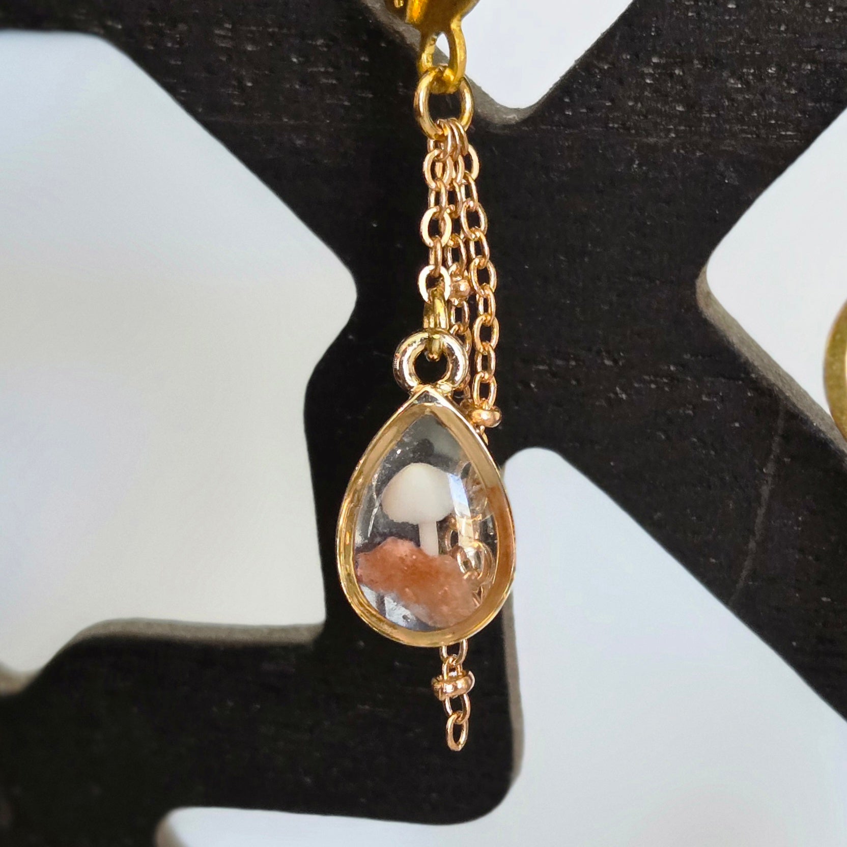 A pair of gold‑tone teardrop earrings containing tiny mushrooms and botanical elements suspended in clear resin.