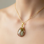 A teardrop resin pendant containing two small white mushrooms, green and gold flakes, and pink stones, hanging from an 18‑inch gold‑tone chain.