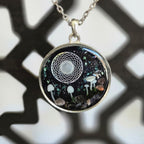 A larger round resin pendant with a dark glittering background, tiny mushrooms, stones, and a white celestial motif surrounding a central sphere, hanging from a 24‑inch silver‑tone chain.