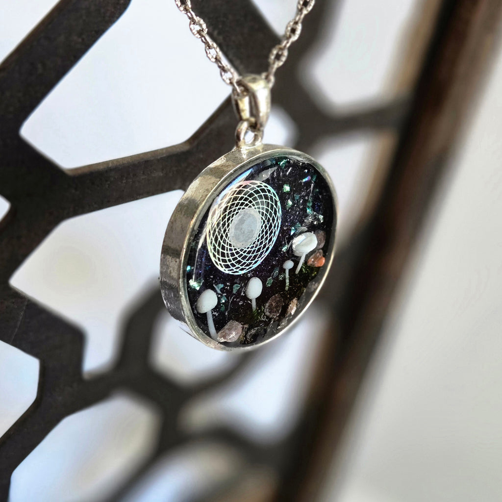 Necklace with a round pendant featuring a black background with white and gray elements, hanging against a blurred background.