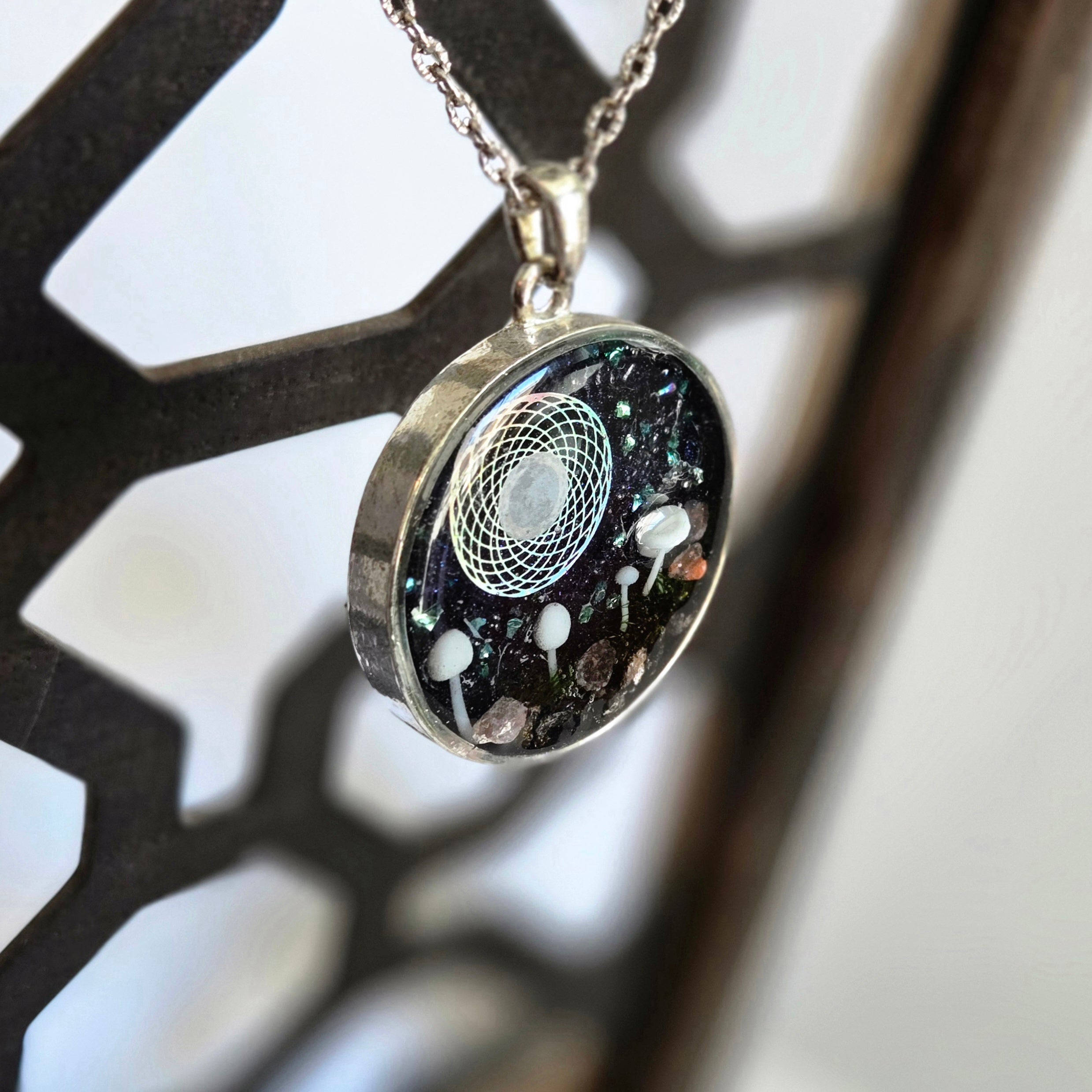 Necklace with a round pendant featuring a black background with white and gray elements, hanging against a blurred background.