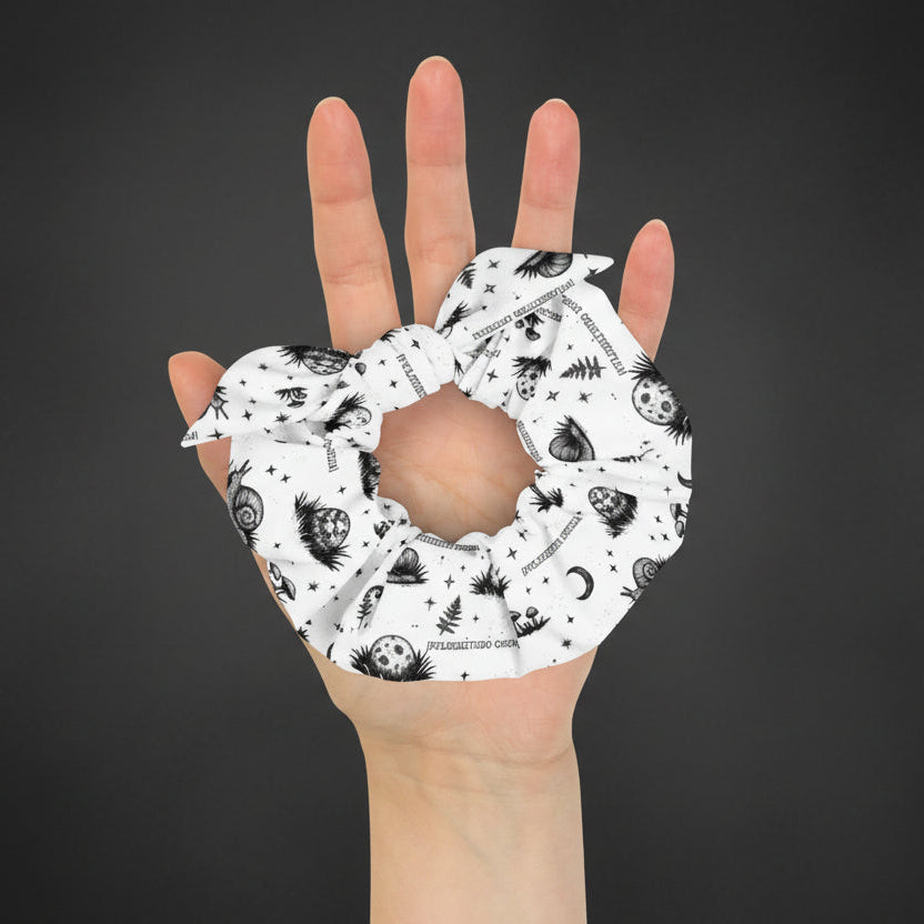 Hand holding a white scrunchie with black patterns on a white background
