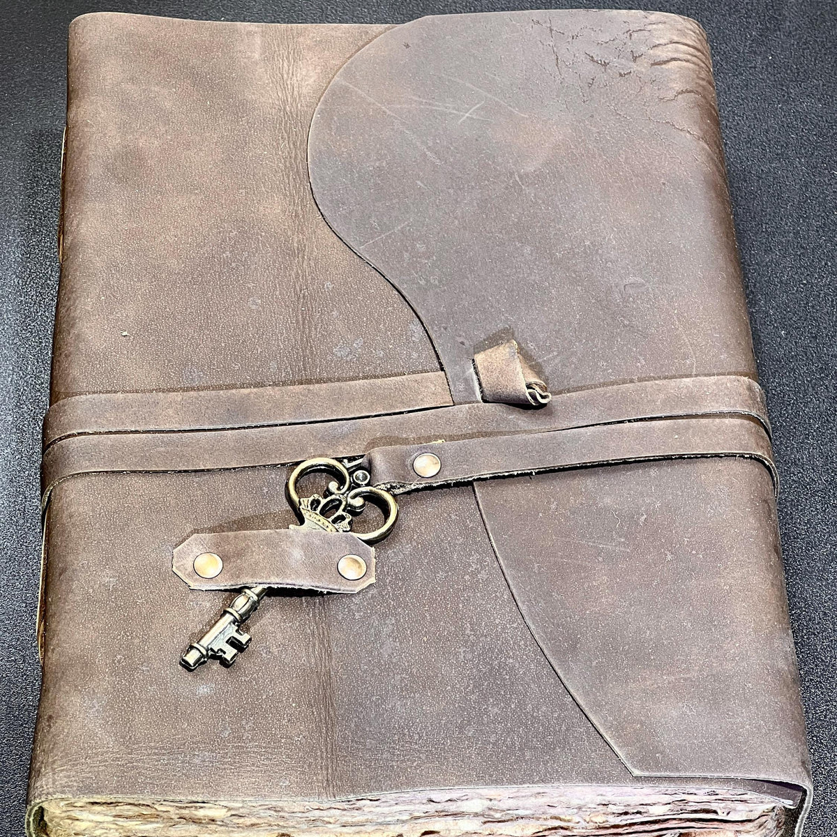 Brown leather-bound book with decorative key locks on a dark background